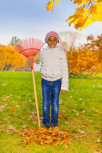 African smiling girl holds red rake and standing in the autumn park during daytime
