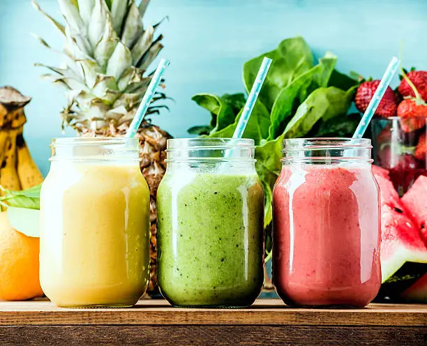 Freshly blended fruit smoothies of various colors and tastes  in glass jars. Yellow, red, green. Turquoise blue background