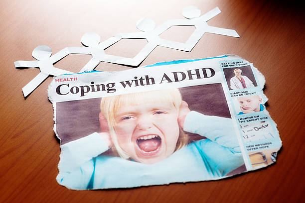 "Coping with ADHD" headline shows screaming little girl Newspaper headline shows a yelling little girl and the headline: "Coping with ADHD". A paper chain of little people sits behind it on a wooden surface. Attention deficit disorder can be a real challenge. front page stock pictures, royalty-free photos & images