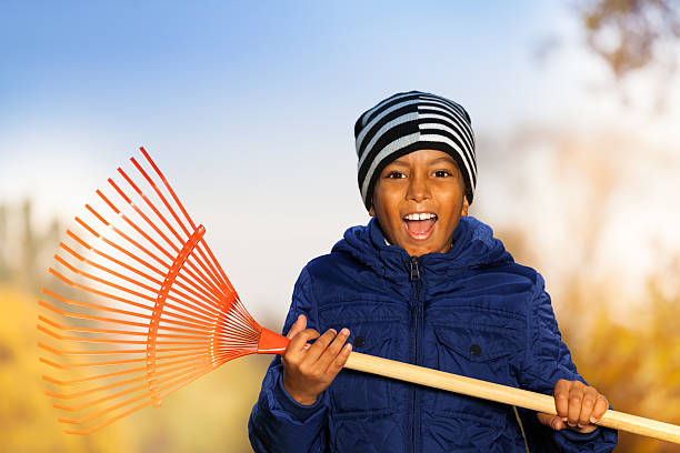 African smiling boy holds red rake with emotions during autumn season