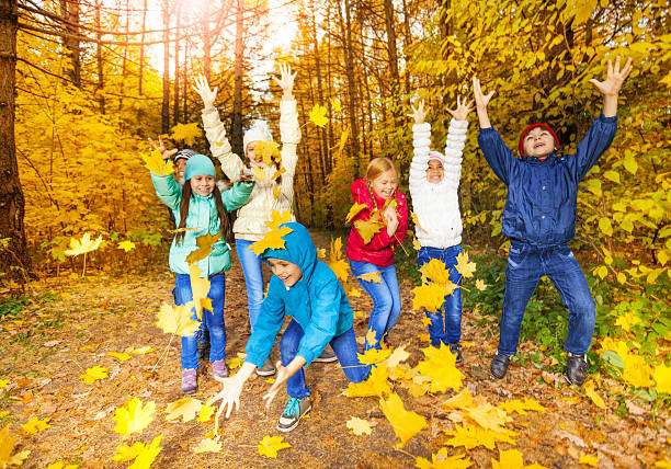 Happy group of children playing together throwing flying yellow leaves in forest during autumn daytime