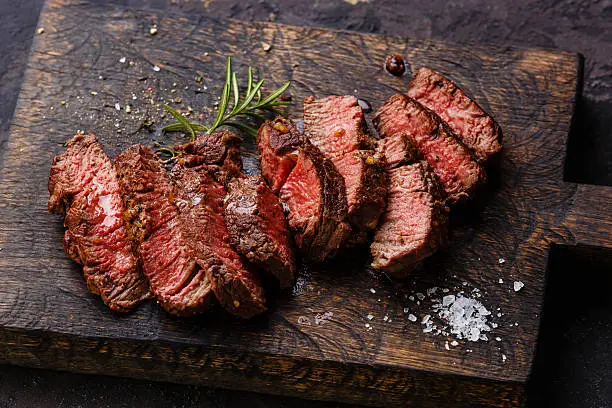 Sliced grilled steak roastbeef and rosemary on wooden cutting board background