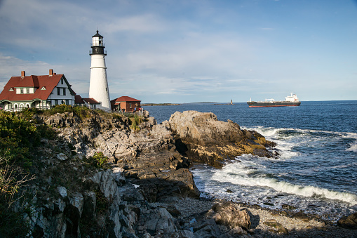 View of the landmark Portland head lighthouse in Maine as a ocean freighter approaches.