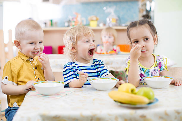 istock Funny little kid with open mouth eating in kindergarten group 527687090