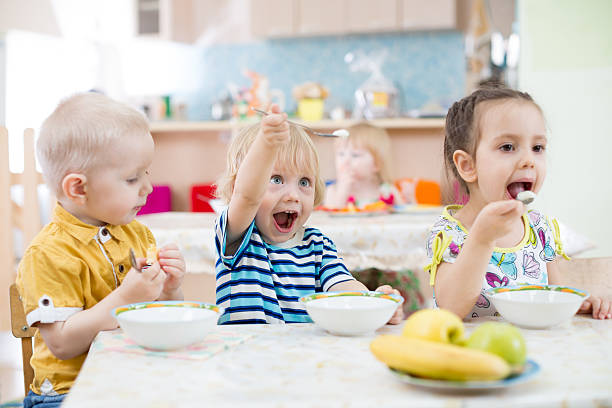 Funny little kid playing and eating in kindergarten funny kids group eating in kindergarten  school lunch child food lunch stock pictures, royalty-free photos & images