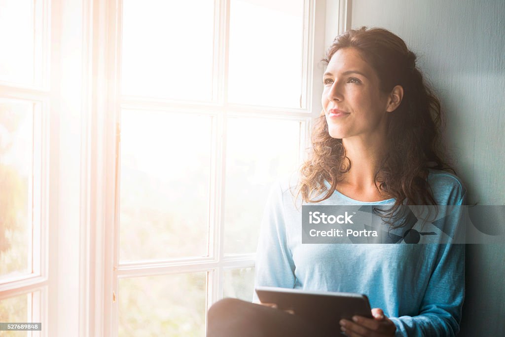 Aufmerksame Junge Frau hält Digitaltablett am Fenster - Lizenzfrei Frauen Stock-Foto
