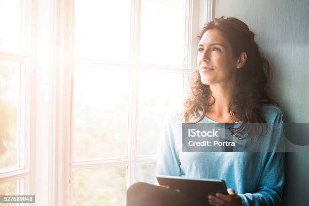 Aufmerksame Junge Frau Hält Digitaltablett Am Fenster Stockfoto und mehr Bilder von Frauen