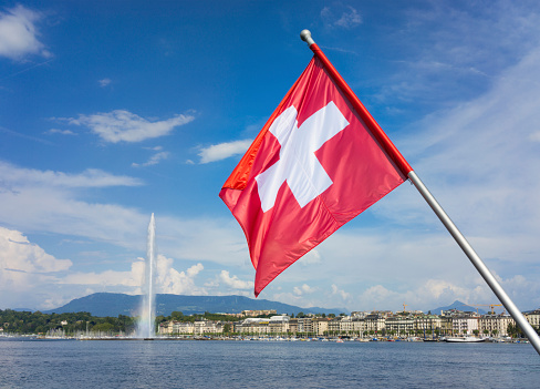 The white cross on red of the Swiss flag in Geneva, with Lake Geneva and the Jet d'eau fountain in the background.