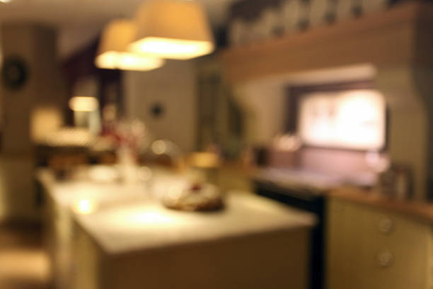 Luxury home domestic kitchen, evening scene, with table, cabinets and equipment: out of focus interior background. Blurred image allows multiple uses as a base or background for more graphic elements.