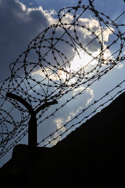 istock Dramatic clouds behind barbed wire fence on a prison wall 527690758