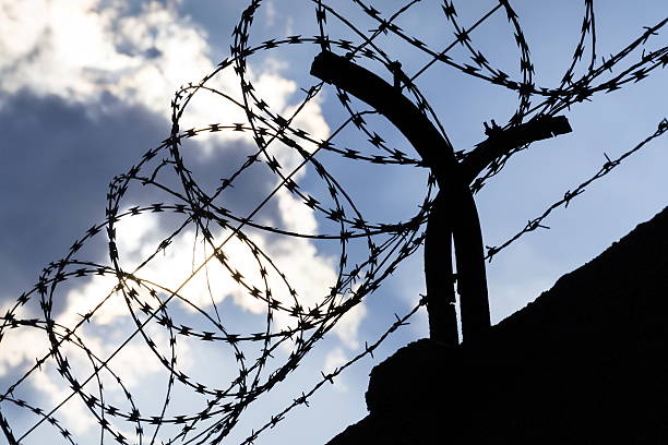 istock Dramatic clouds behind barbed wire fence on a prison wall 527690840