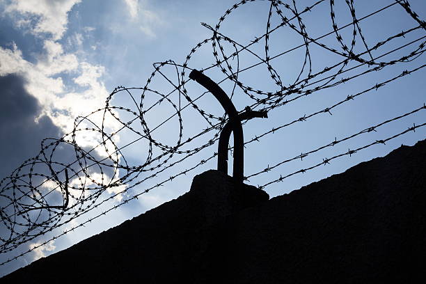 istock Dramatic clouds behind barbed wire fence on a prison wall 527691132