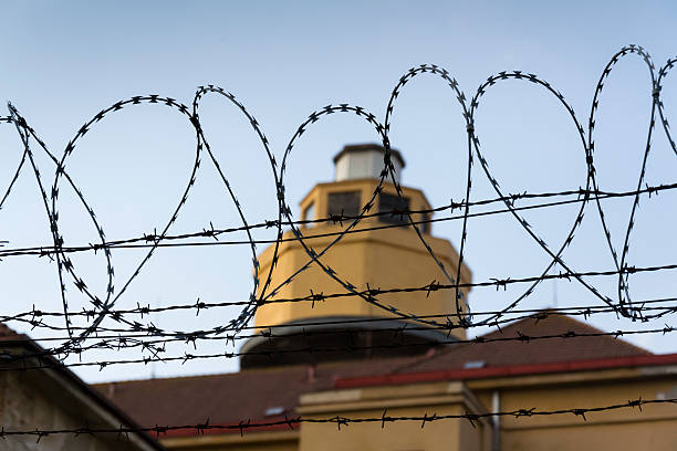 istock Guarding tower behind barbed wire fence around prison walls 527691552