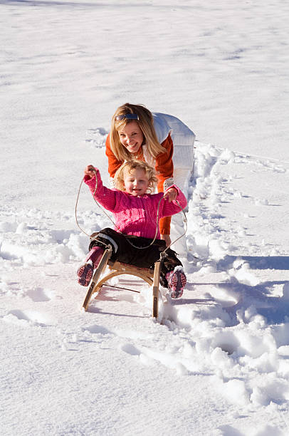 istock Girl sitting on sledge, mother pushing 527708529