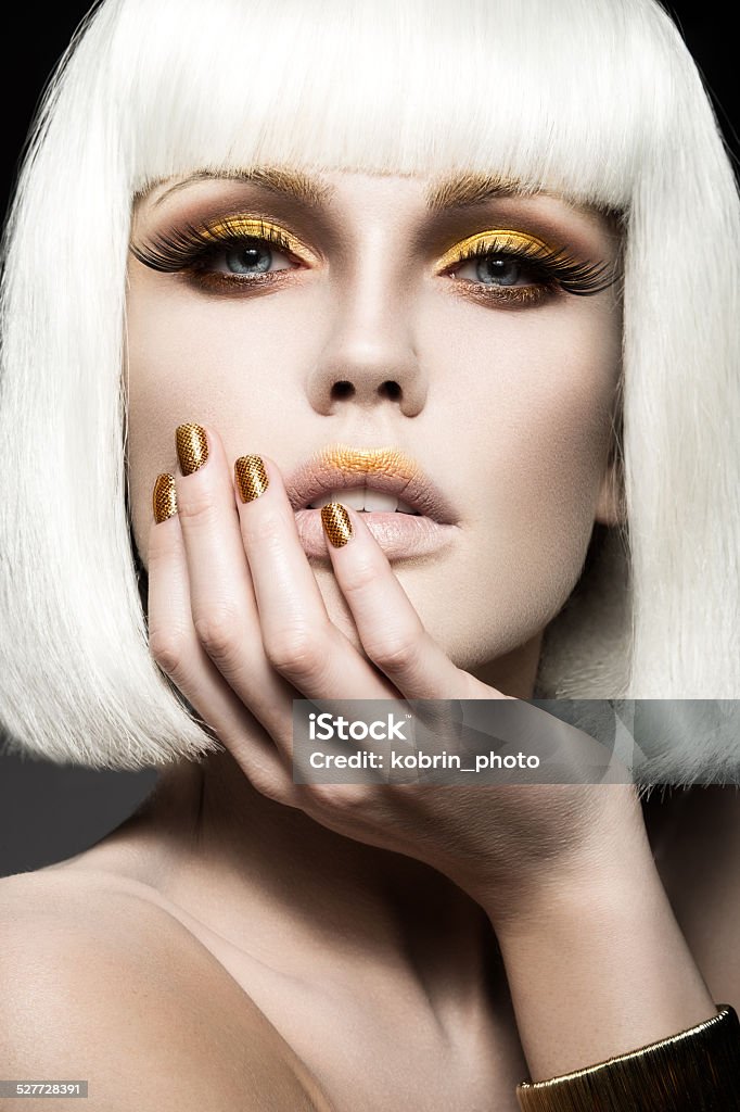 Beautiful girl in white wig, with gold makeup and nails. Beautiful girl in a white wig, with gold makeup and nails. Celebratory image. Beauty face. Picture taken in the studio. Fashion Model Stock Photo