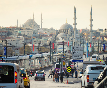 Traffic and pedestrians near on the Galata Bridge over the Golden Horn, with the mosques and traditional architecture of Istanbul's Old City in the background.
