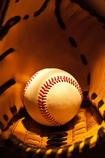 Photo of Base ball held in glove, isolated on a dark background
