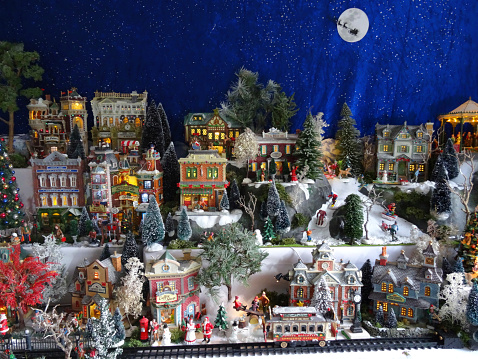 Frome, Somerset, England, UK - December, 10 2014: Seasonal concept photo showing a magical model Christmas village scene in winter set up in the conservatory of my house, using a large table, wooden staging and white polyester fleece to create a blanket of snow.  The model village recreates a detailed winter's scene in miniature and comes complete with miniature ceramic buildings and houses, realistic plastic, hand-painted people and scale figurines, tiny battery-powered fairy lights (all made by Lemax) and lots of fake snow powder.