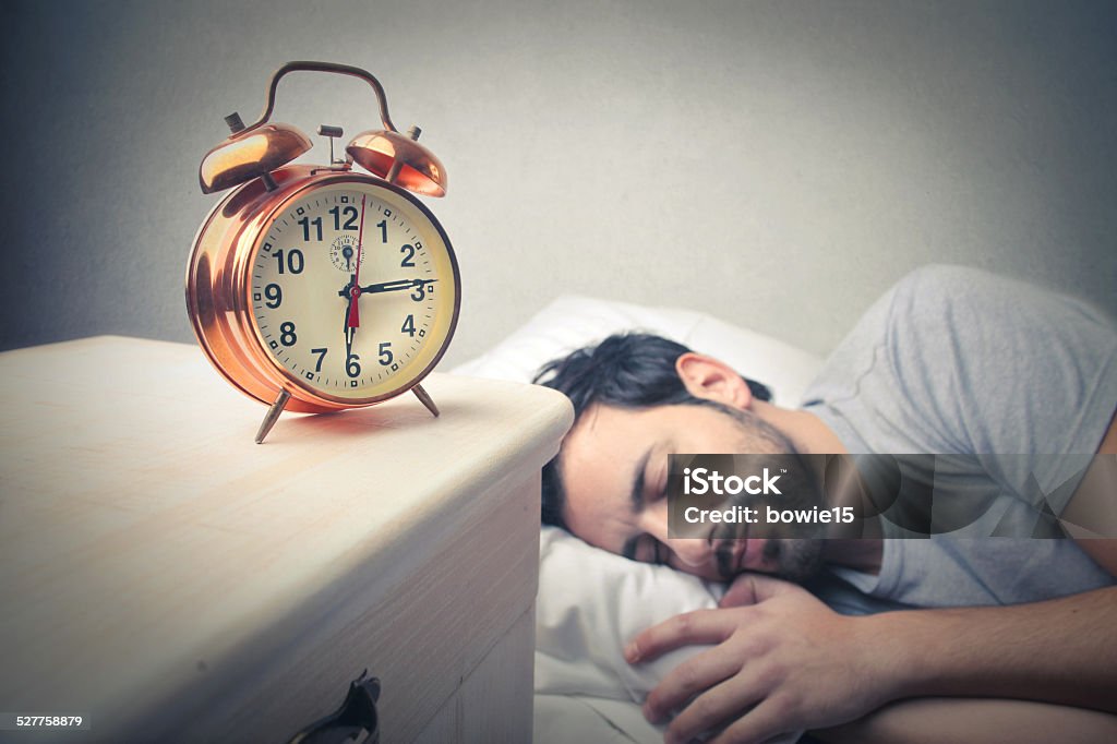 Alarm clock In the background a man is sound asleep; in the foreground an alarm clock Adult Stock Photo
