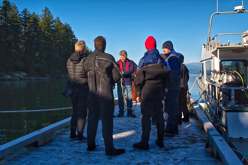 a group of commercial diving students are gathered together on a dock on a frosty winter morning for a pre-dive lecture
