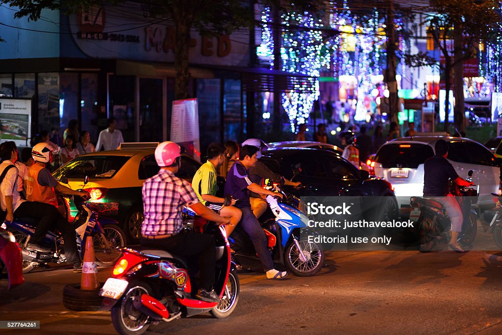 Driving motorscooter at night in Bangkok Bangkok, Thailand - November 6, 2014: Capture of traffic on Wanghin Road in Bangkok Ladprao at night. Queued traffic of cars, taxis and some motorcycles. On motorcycles are thai people and at left side is thai motorcycle taxi driver. Other people are on sidewalk in background. Asphalt Stock Photo