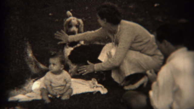 1936: Mom blocking protecting baby from fighting dogs outdoor picnic.