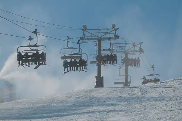 Alpine skiers on a chairlift with snow making in the background