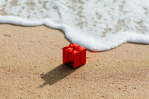 present gift in red box  on the beach in tropics. Present red box flowing in the sea. christmas holideys on the beach