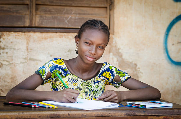 African School Girl Posing for an Educational Shot Symbol Portrait of an African ethnicity schoolgirl (age 13) in an educational environment in Bamako, Mali learning her lesson outdoors sitting on a desk and slightly smiling. mali stock pictures, royalty-free photos & images
