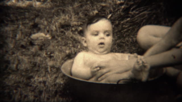 1936: Newborn baby bath washed in a cooking pot outdoor.