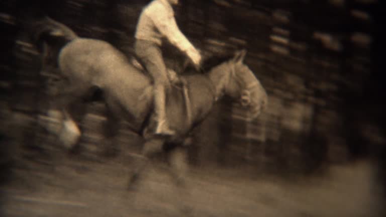 1937: Men jumping horses over fence loses hat in wooded rural area.