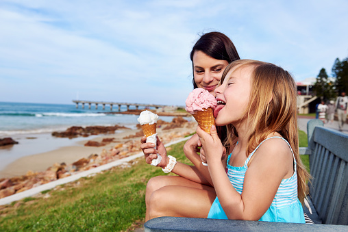 Mom and daughter enjoy fun ice cream at the beach smiling laughing joy on summer vacation