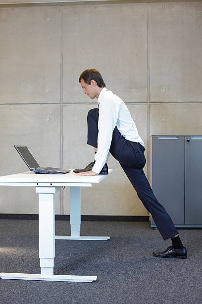 istock business man stretching leg in standing position at desk 527842791