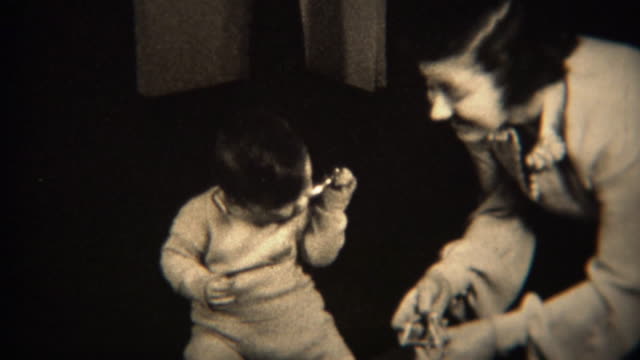 1937: Caring mother and baby unwrap gift together, drops doll on floor.