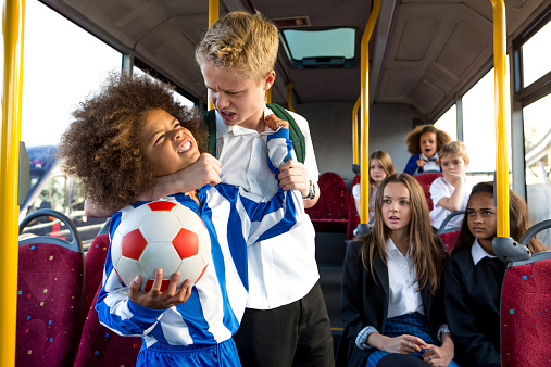 School bully on bus holding another pupil in a headlock as other students watch.