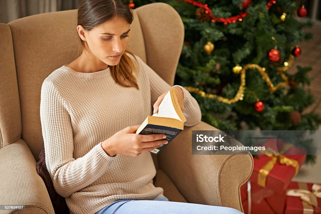 Can't put a good book down Shot of a beautiful young woman reading a book at home during the Christmas holidays Adult Stock Photo