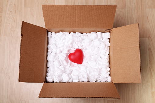 Cardboard box with packing peanuts and a red heart inside
