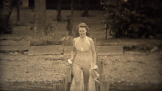 1938: Cute woman walking on lake dock in conservative 30s style swimwear.
