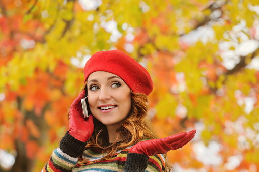 portrait of beautiful attractive young woman talking on the phone in autumn park, fall concepr background