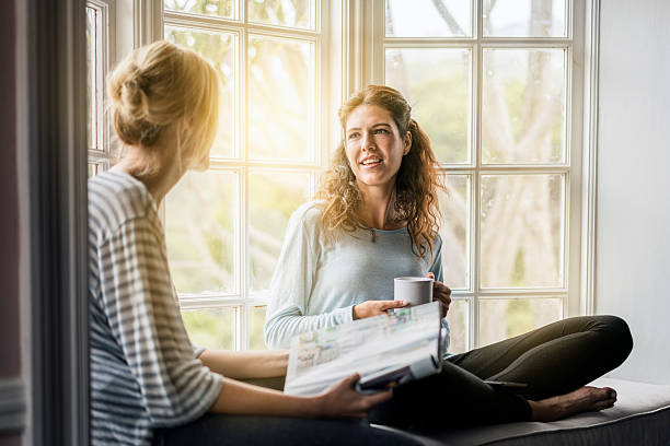 Young female friends talking on window sill