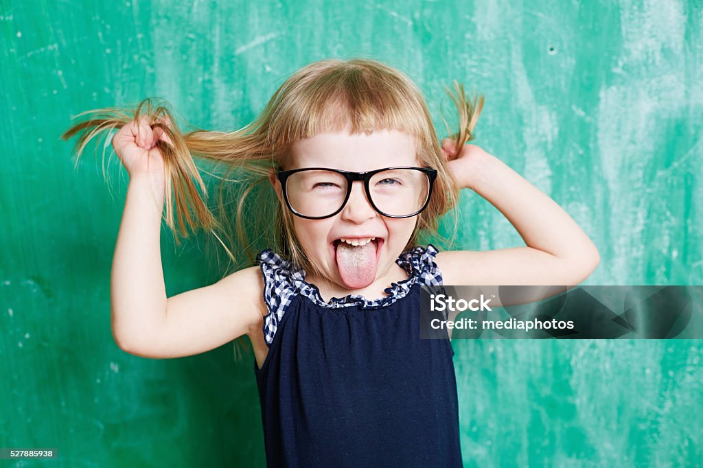 Naughty sweetie Naughty preschooler grimacing against blackboard Sticking Out Tongue Stock Photo