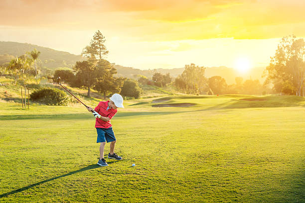 молодой мальчик играет в гольф. teeing во время заката - child swing swinging balance стоковые фото и изображения