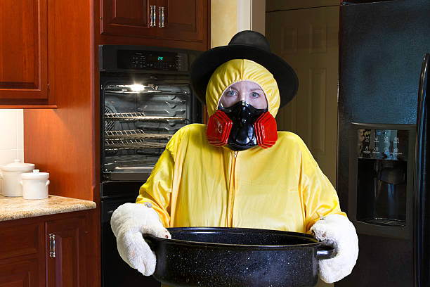 Thanksgiving Dinner Disaster with HazMat Suit Woman in yellow HazMat suit and respirator wearing Pilgrim hat standing next to open oven in kitchen. thanksgiving holiday covid stock pictures, royalty-free photos & images