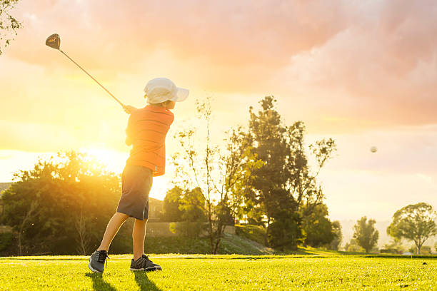 muchacho joven golfista golpear desde el tee durante la puesta del sol - nivel júnior fotografías e imágenes de stock