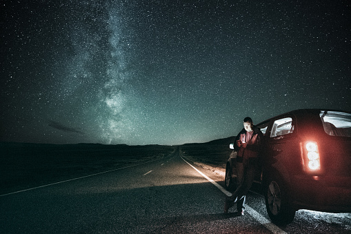 Driver takes a break on a lonely road under the milky way.