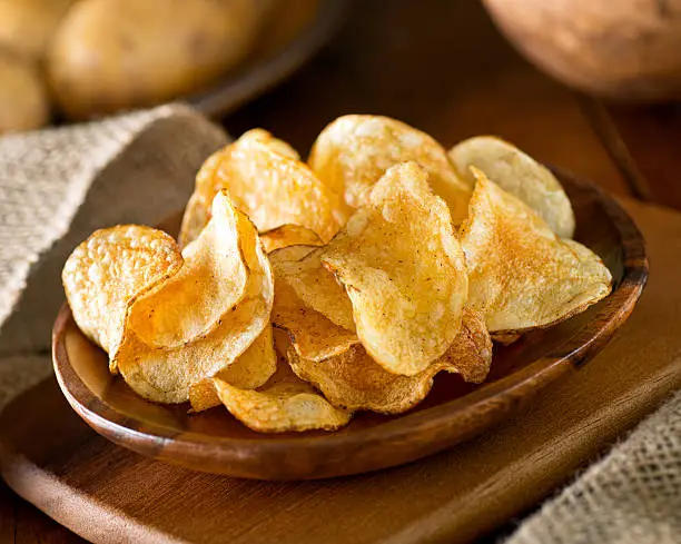 Delicious home made potato chips with sea salt and black pepper against a rustic background.