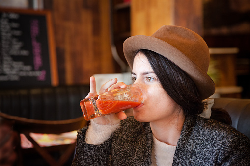 quirky girl with trilby hat enjoys tomato juice in cafe