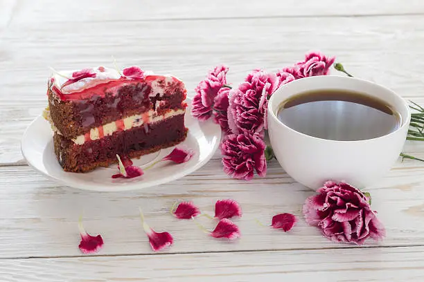 Red velvet cake, cup of coffee and pink carnations on wooden table