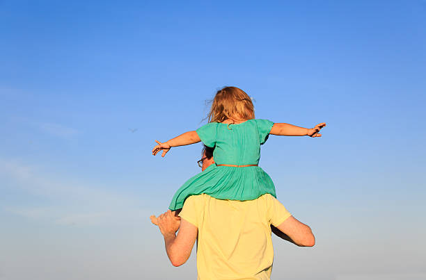 istock father and little daughter on shoulders play at sky 527909024