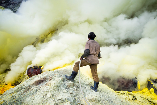 Kawah Ijen Volcano, East Java, Indonesia - May 25, 2013: Sulfur miner spraying water onto pipes inside the crater of Kawah Ijen volcano in East Java, Indonesia..